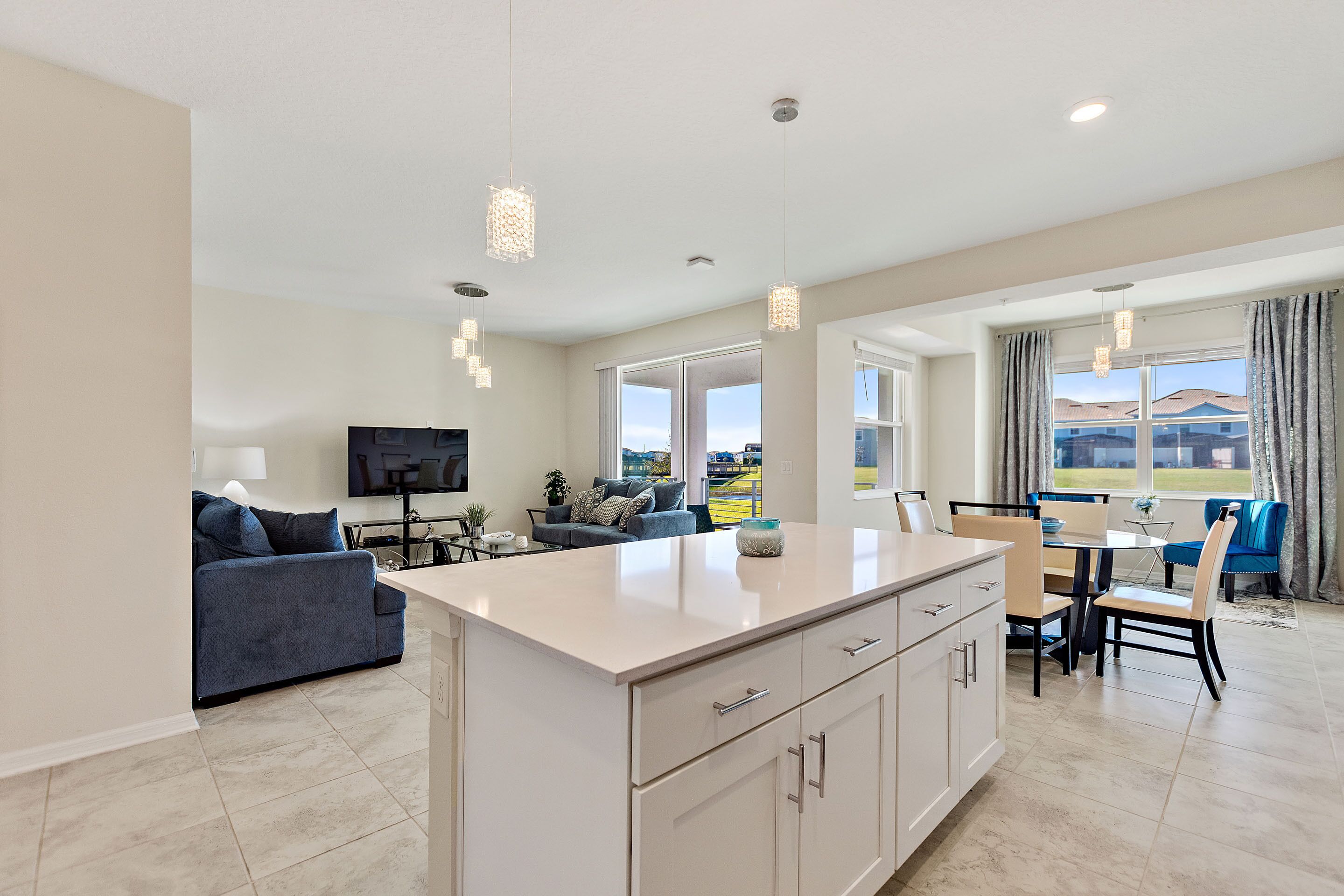 A modern kitchen with a central island, dining area with chairs, a sofa, and a TV.