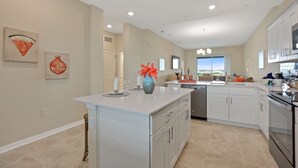 Una cocina amplia con una isla grande, muebles blancos y vistas al exterior.