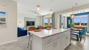 Cozinha moderna com ilha central, espaço de jantar e sala de estar com sofá azul e televisão.