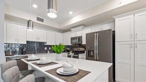 A modern kitchen with white cabinets, stainless steel appliances, a central island with seating, and a potted plant. - Storey Lake 2 Bed, Sleeps 7. Premium, Fabulous #200 (Kissimmee)