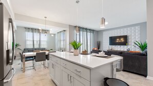 A modern kitchen with a central island, dining area, and a living space with a sofa and TV. - Storey Lake 2 Bed, Sleeps 7. Premium, Fabulous #200 (Kissimmee)