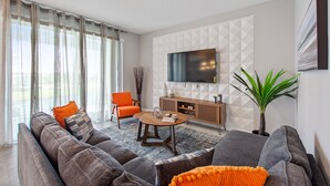 A modern living room with a grey sofa, orange cushions, a wooden coffee table, and a TV mounted on the wall. - Storey Lake 2 Bed, Sleeps 7. Premium, Fabulous #200 (Kissimmee)