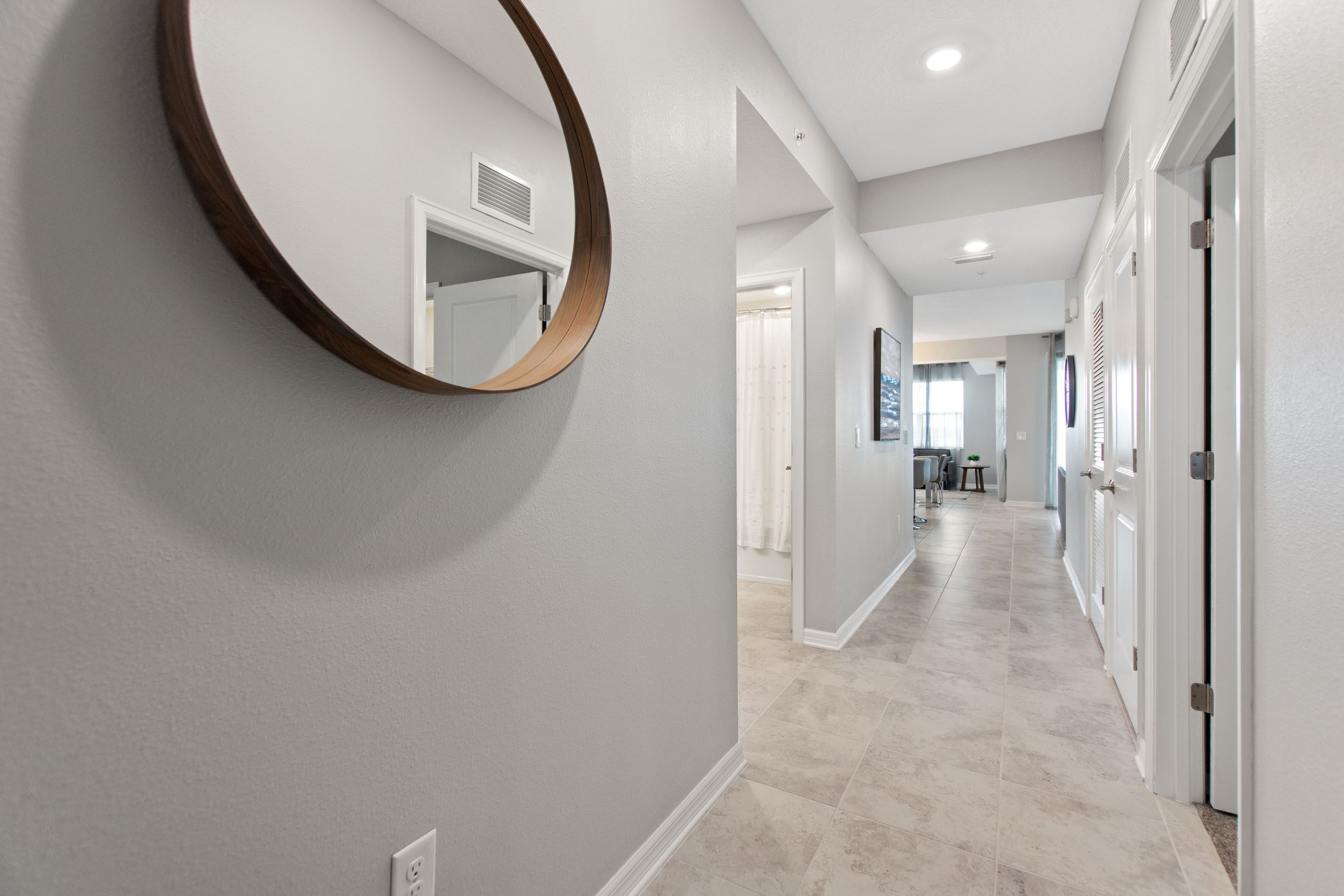A hallway with a round mirror, light gray walls, and a tiled floor.