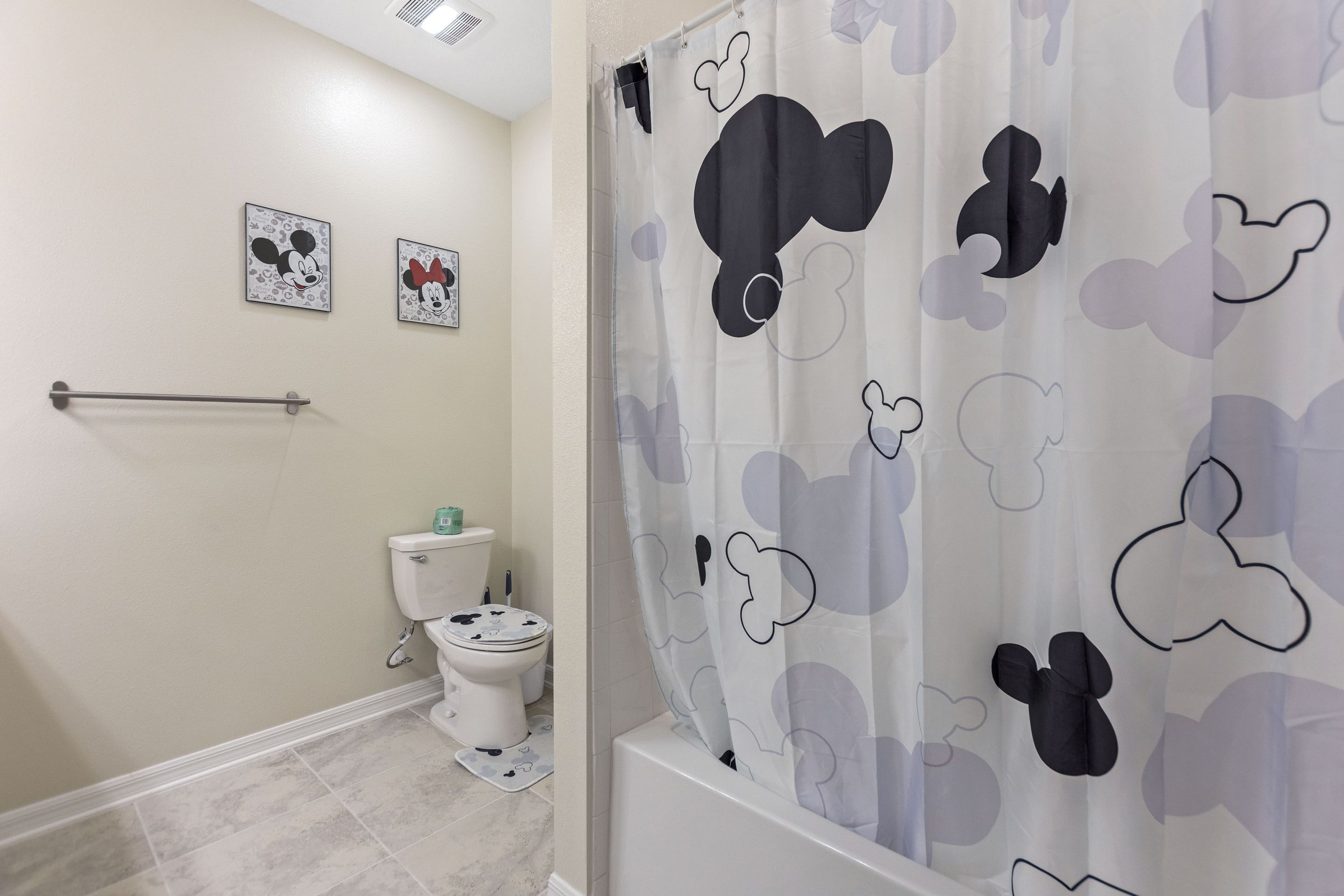 Une salle de bain avec un rideau de douche à l’effigie de Mickey Mouse, des toilettes et deux tableaux encadrés représentant Mickey Mouse accrochés au mur.