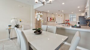 A modern kitchen with white cabinets, a central island, and a dining area with a white table and chairs. - Ripples at Storey Lake by Shine Villas #905 (Kissimmee)