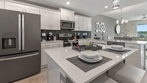 A modern kitchen with white cabinetry, stainless steel appliances, and a central island with seating. - Ripples at Storey Lake by Shine Villas #905 (Kissimmee)