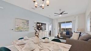 A modern dining area with a marble table set for four, a chandelier, and a ceiling fan. - Edgewater Escape at Storey Lake by Shine Villas #904 (Kissimmee)