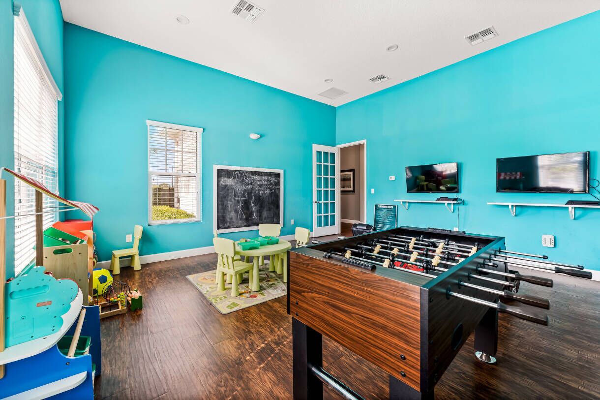 A room with teal walls, a foosball table, a chalkboard, and a television.