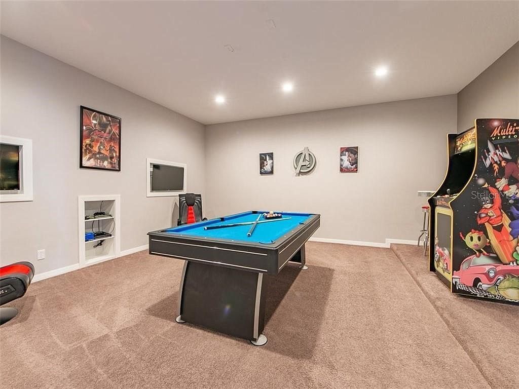 A room with a pool table, a television, and arcade games.