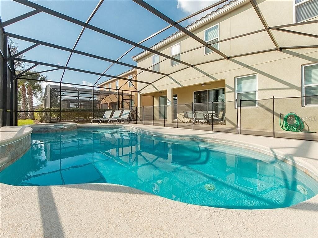 Une piscine dotée d’une structure en verre, de chaises longues et d’un bâtiment à la façade beige.