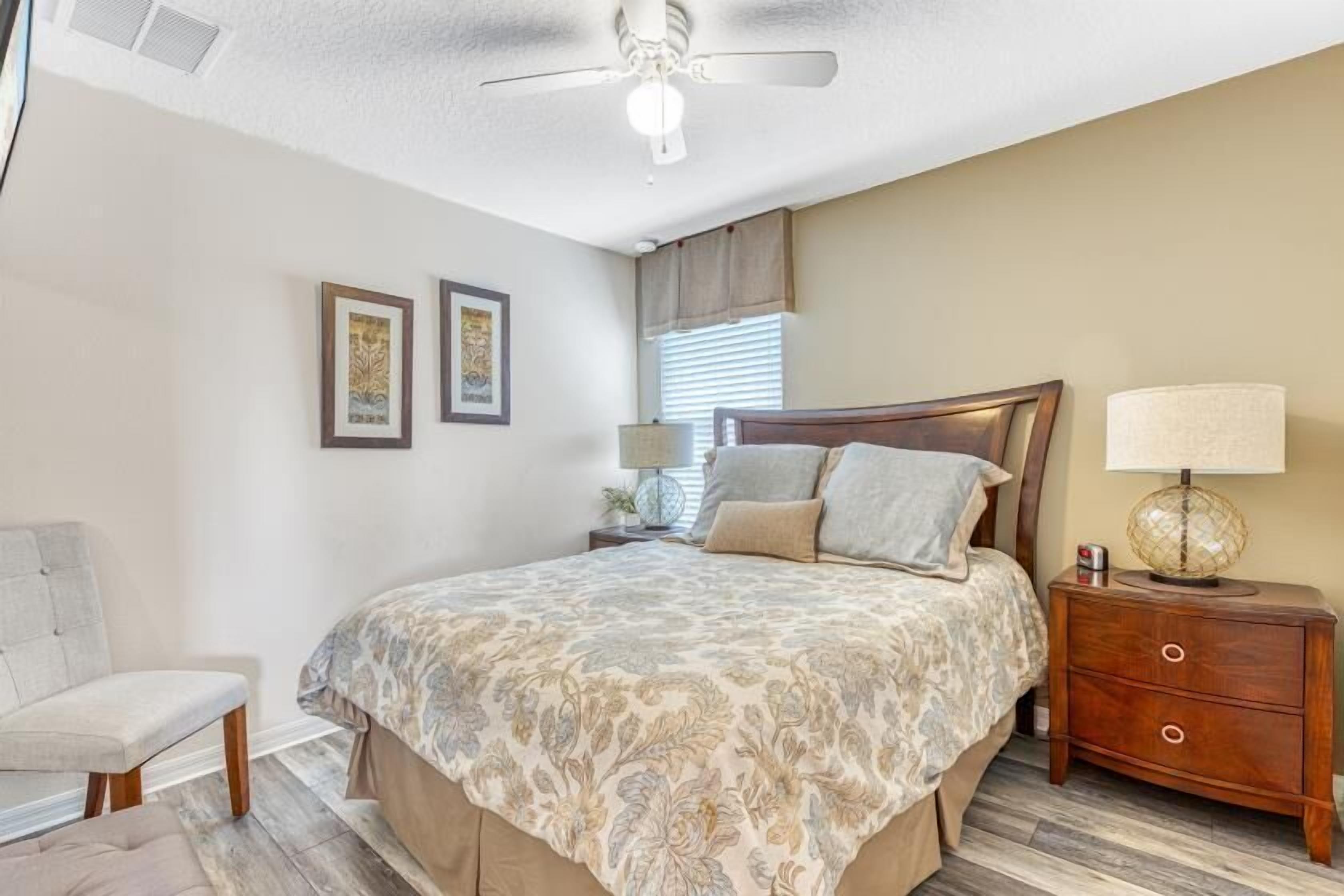A bedroom with a bed, a chair, a nightstand, a lamp, and two framed pictures on the wall.