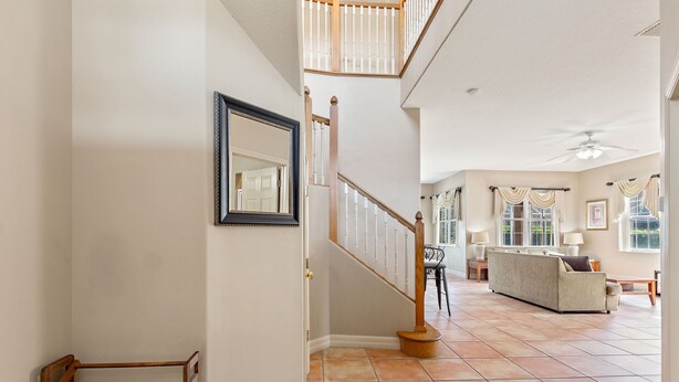 A spacious living area with a high ceiling, a staircase with a wooden railing, and a large window allowing natural light. - 6 Bedroom Premium Home With Pool, Spa and Games Room #800 (Davenport)