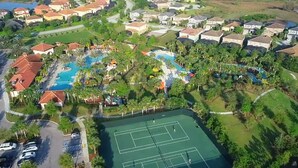 Vue aérienne d’un quartier résidentiel avec une piscine, des courts de tennis et des maisons.