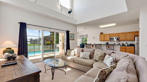 A spacious living room with a large sofa, a glass coffee table, and a view of a pool through a sliding glass door.