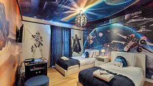 Ein Zimmer mit zwei Betten, einem Deckenprojektor und Wandbildern zum Thema Weltraum.