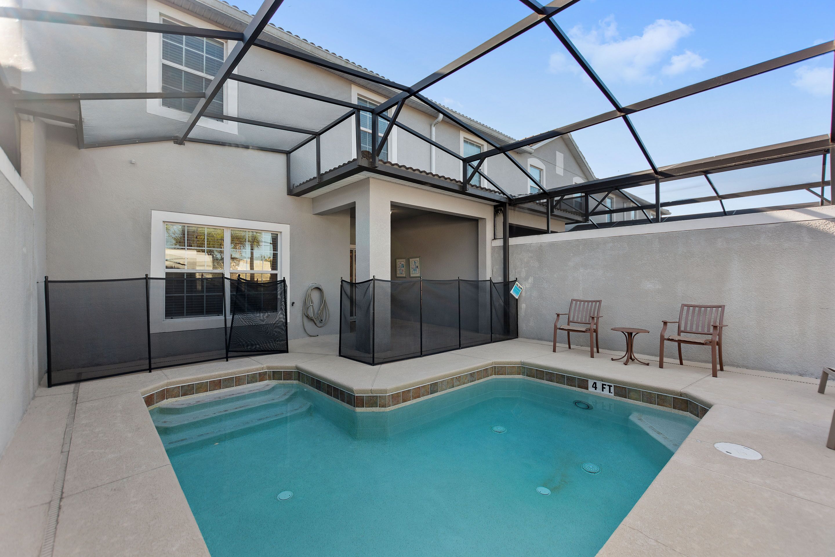 A swimming pool with a 4 ft. depth marker, surrounded by a covered patio area with chairs and a table.
