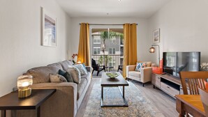 A modern living room with a sofa, coffee table, TV, and a view of the outside balcony. - Contemporary @vista Cay By Shine Villas #403 (Orlando)