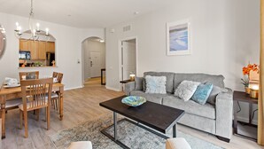 A modern living room with a grey sofa, wooden dining table, and a black coffee table. - Contemporary @vista Cay By Shine Villas #403 (Orlando)