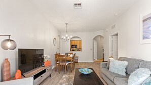 A modern living room with a TV, sofa, dining table, and chairs. - Contemporary @vista Cay By Shine Villas #403 (Orlando)
