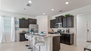 A modern kitchen with dark cabinets, a central island with bar stools, a refrigerator, microwave, and stove.