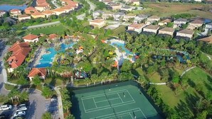 An aerial view of a residential area with a swimming pool, tennis courts, and houses.