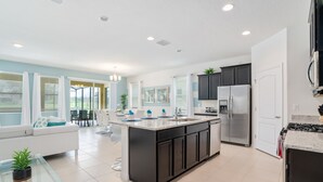 A modern kitchen with a central island, dark cabinetry, stainless steel appliances, and a dining area with a white sofa and glass table.