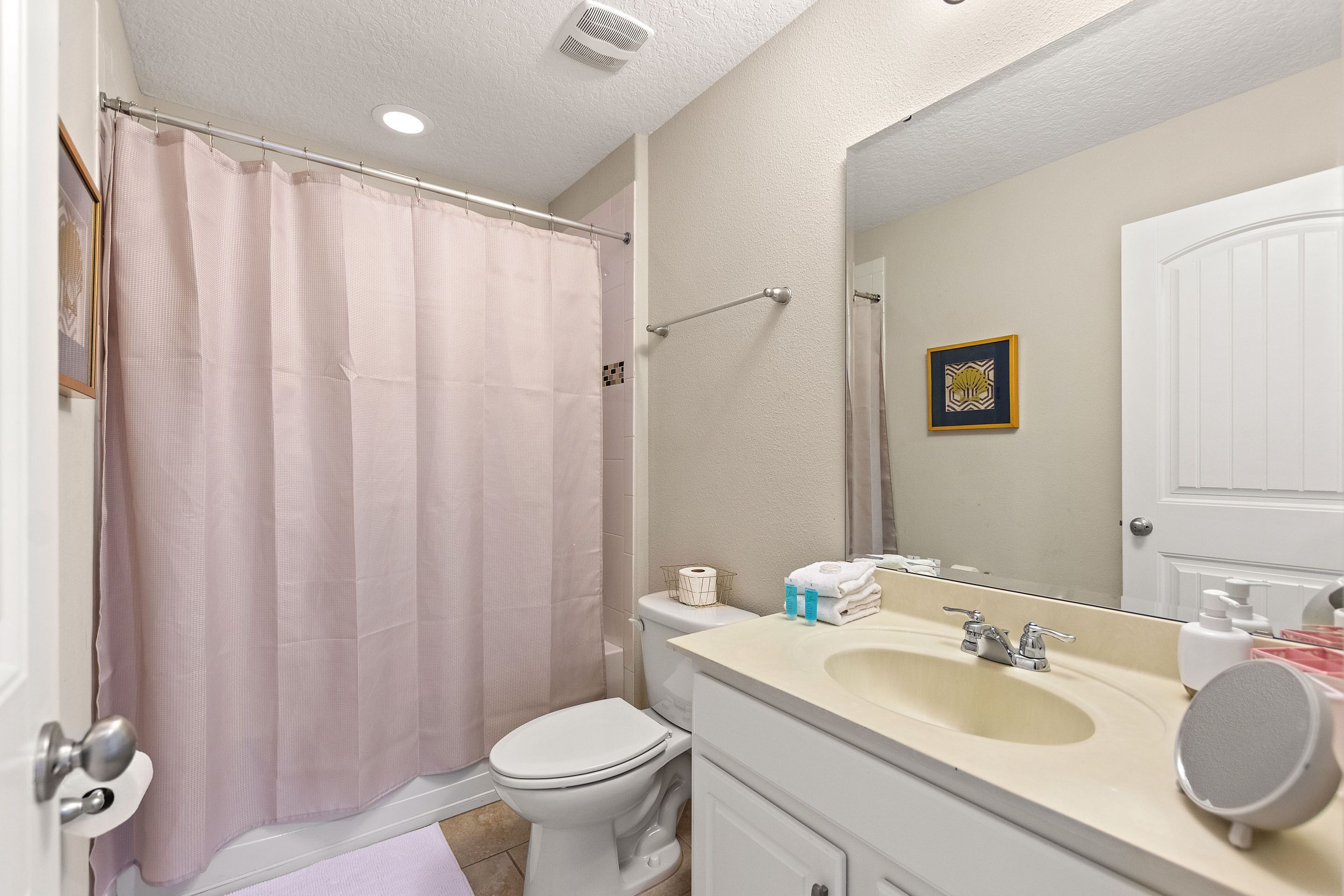 A bathroom with a shower curtain, toilet, sink, and mirror.