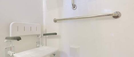 A white bathroom with a white bench, a handrail, and a wall-mounted toilet.