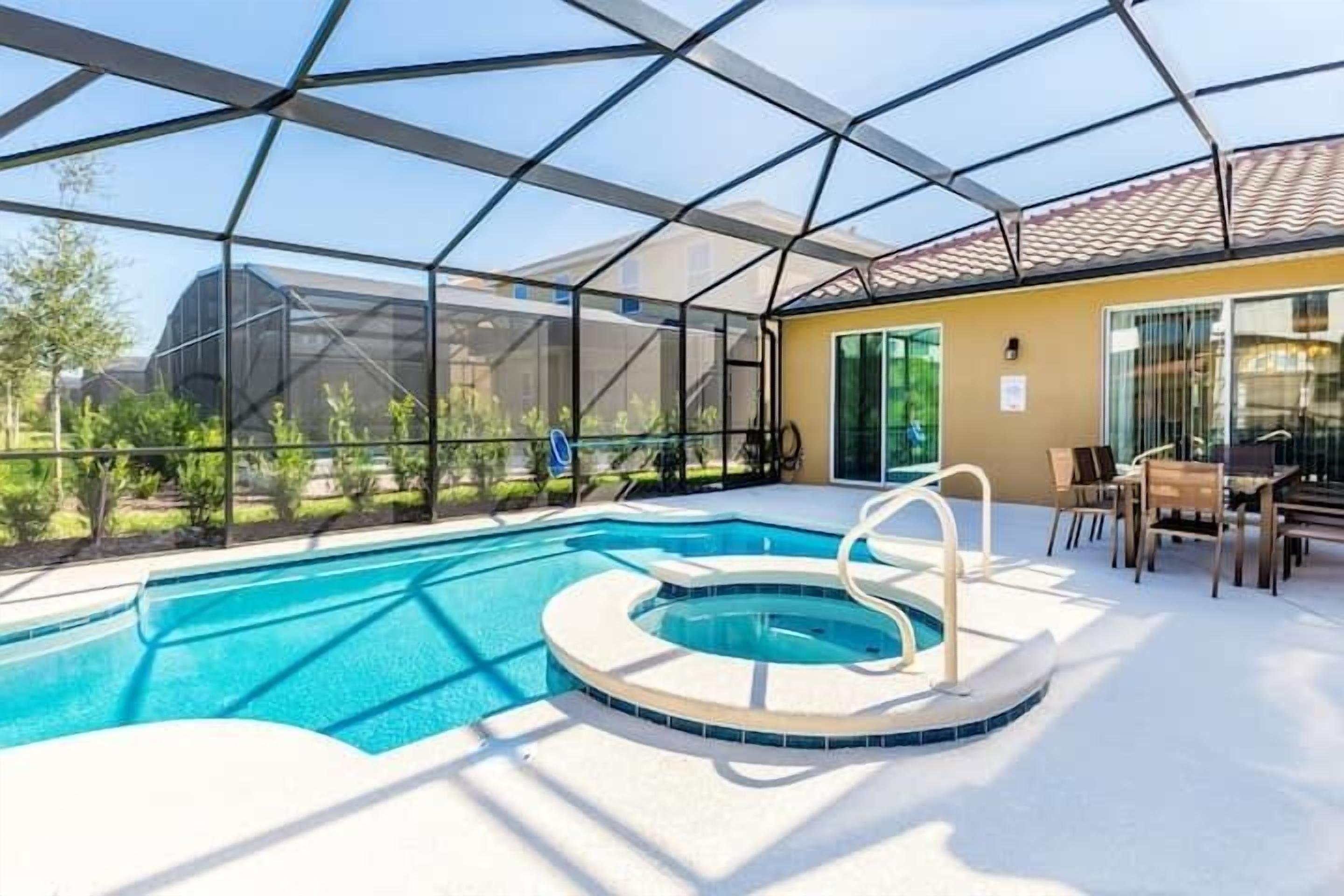 Una piscina con hidromasaje, rodeada por un recinto de vidrio y con mobiliario exterior.