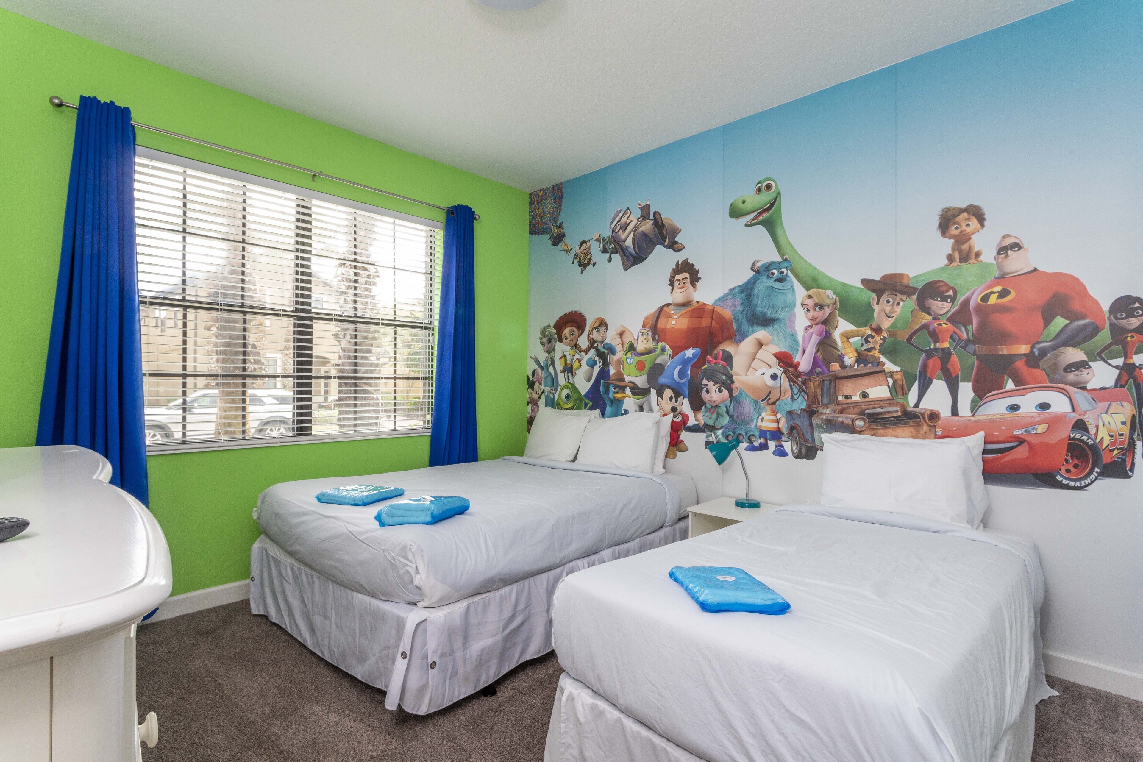 A room with two beds, a desk, and a window with blue curtains.