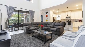 A modern living room with a sectional sofa, a coffee table, and a dining area with a table and chairs. - Brilliance at Solterra Resort by Shine Villas #092 (Davenport)