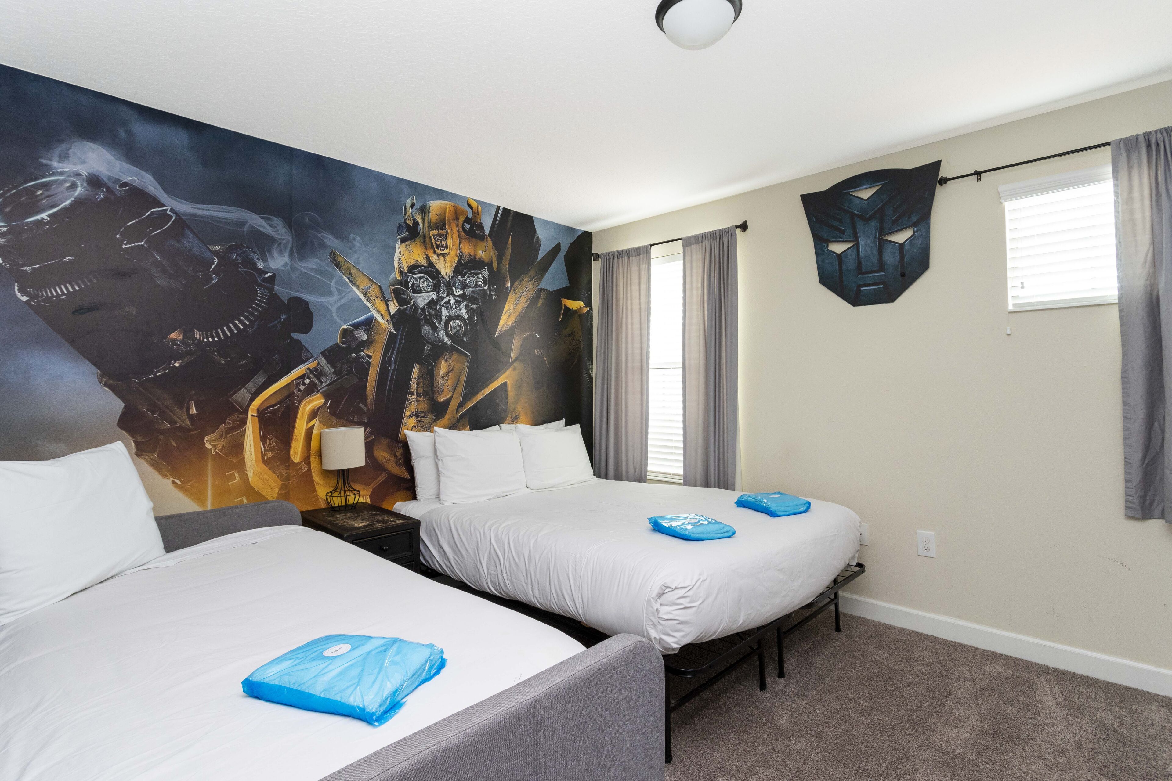 A hotel room with two beds, a mural on the wall, a window with curtains, and a wall-mounted mask.