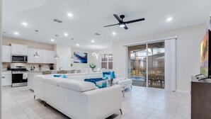 A modern living space with a white sofa, kitchen area, and sliding glass doors leading to an outdoor area. - 5 Bed Bliss at Solterra by Shine Villas 121 (Davenport)