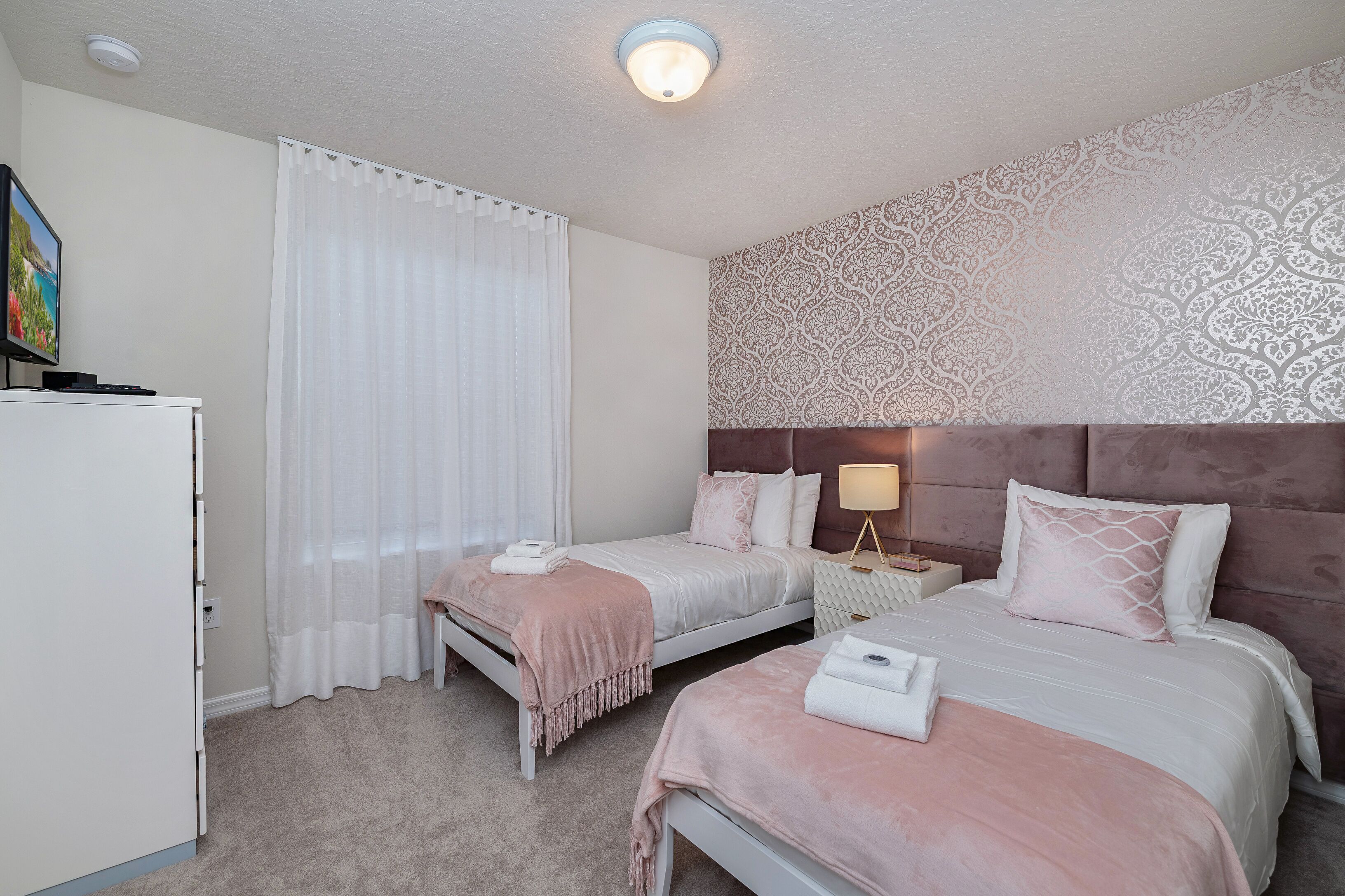 A hotel room with two beds, a wardrobe, a television, and a patterned wall.