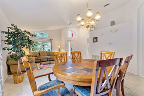 A dining area with a round wooden table and chairs, a chandelier, and a large potted plant. - Emerald Island Resort, Private Pool, Games Rm #823 (Kissimmee)