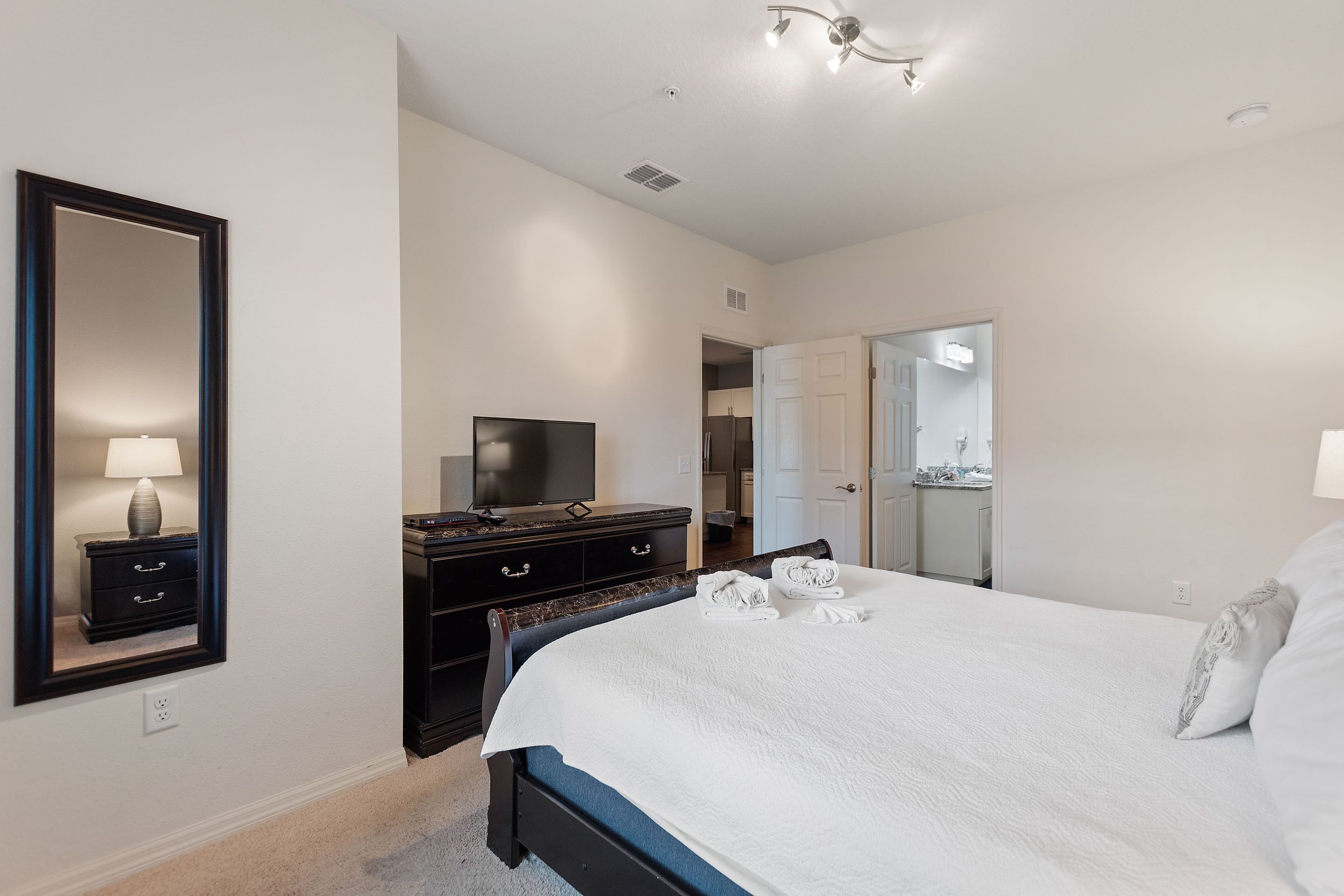 A bedroom with a large bed, a dresser, a television, and a mirror.