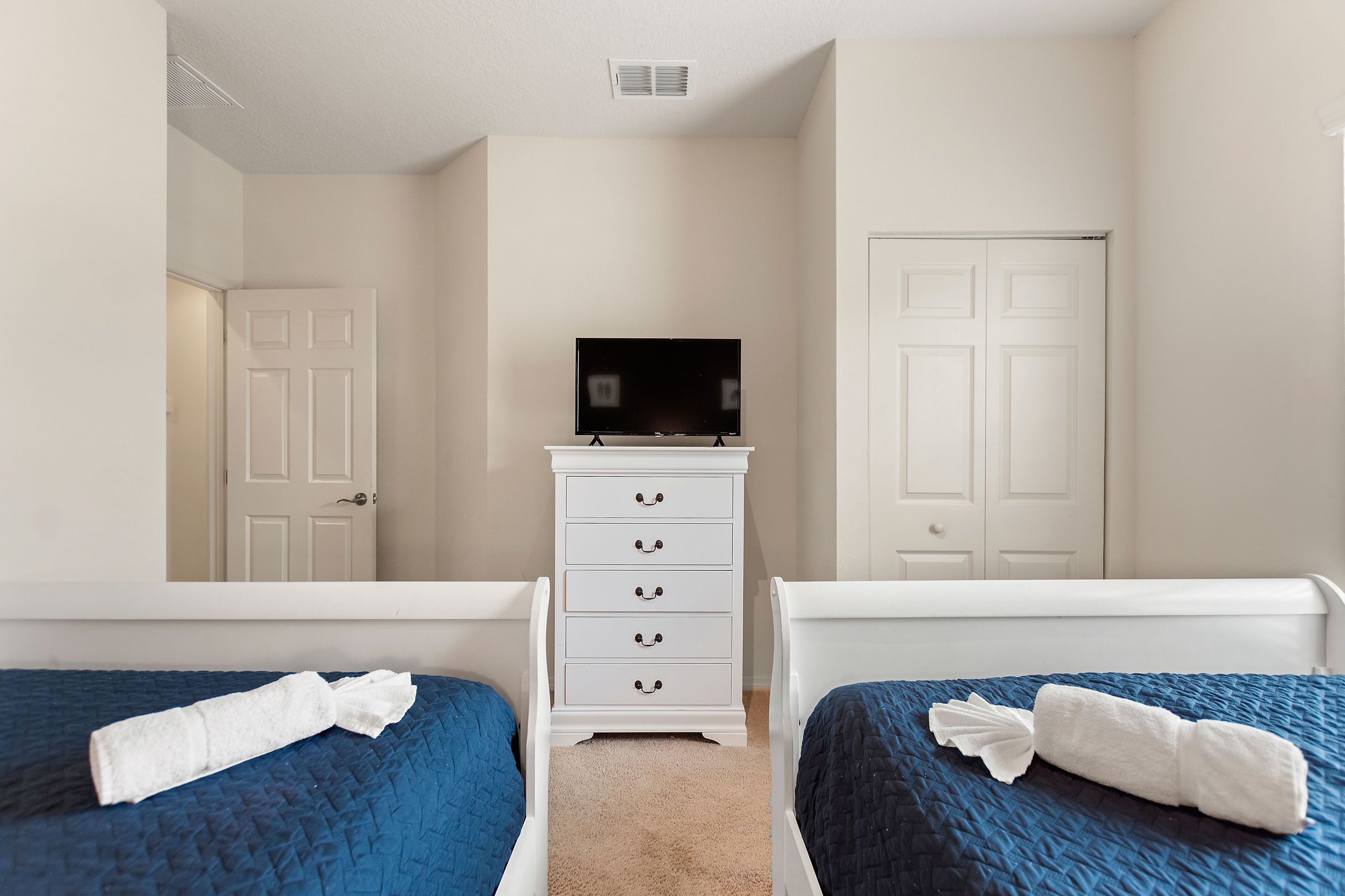 Une chambre d’hôtel avec deux lits simples, une commode blanche, un téléviseur et une porte.