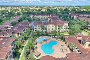 A residential complex with multiple apartment buildings, a central swimming pool, and surrounding greenery. - Sunnyside Up at Bella Piazza by Shine Villas (Davenport)