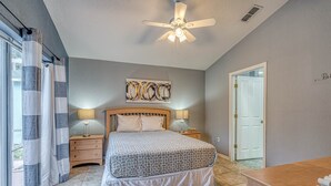 Une chambre à coucher avec un lit, des tables de chevet avec des lampes, un ventilateur de plafond, une porte et une vue sur l’extérieur.