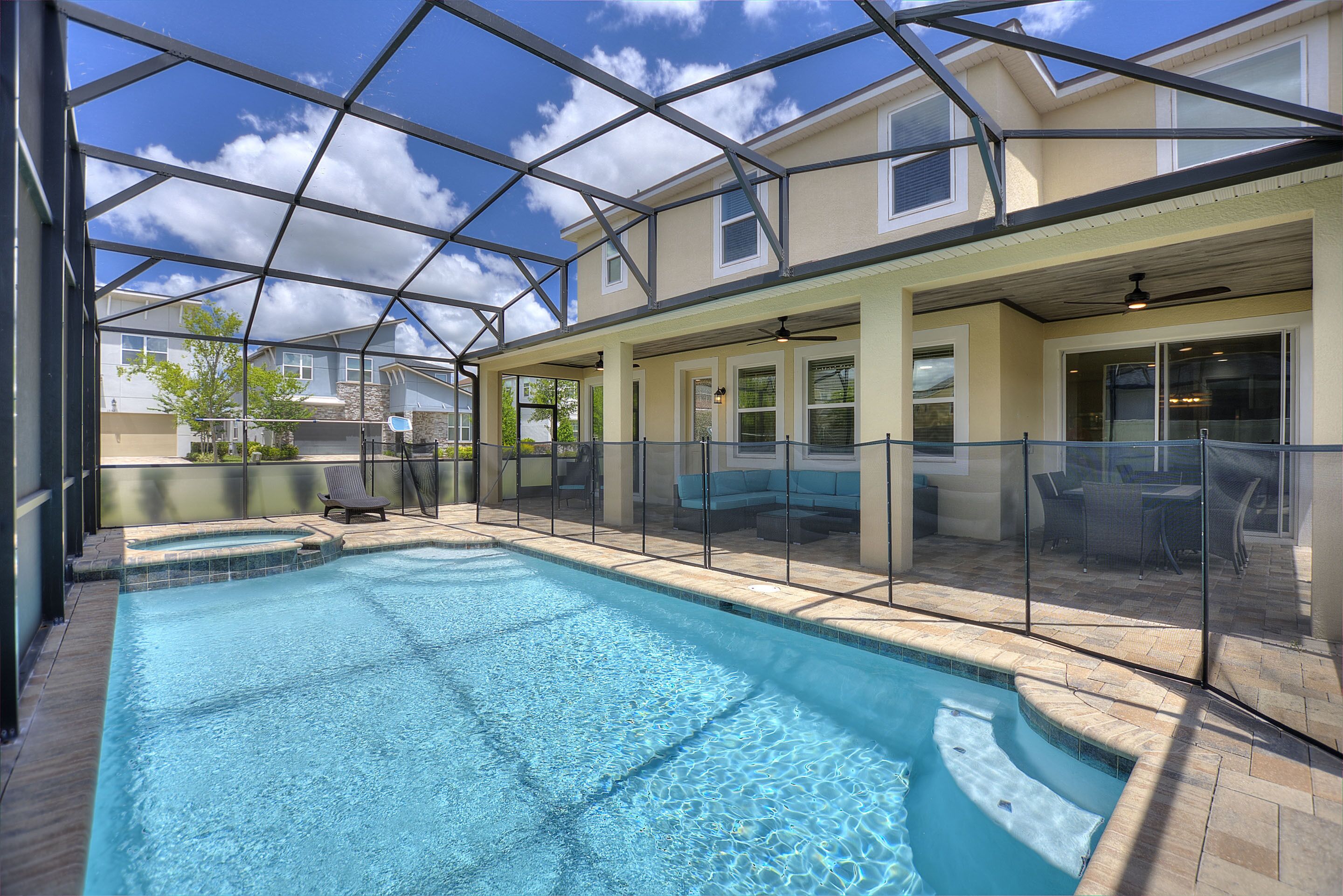 A swimming pool with a glass enclosure, surrounded by outdoor furniture and a covered patio area.