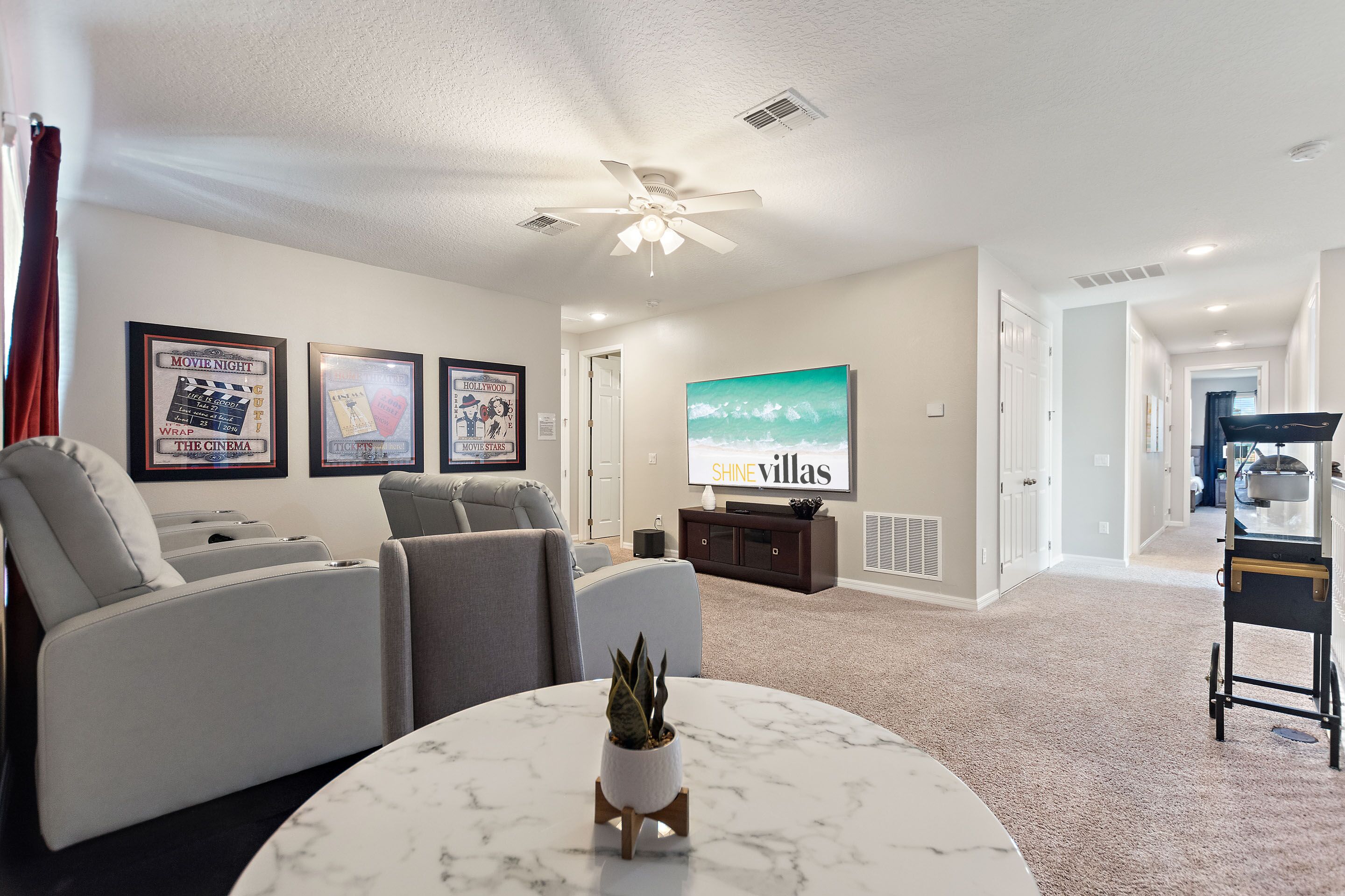 A modern living room with a ceiling fan, a flat-screen TV, a marble coffee table, and a seating area with a sofa and chairs.