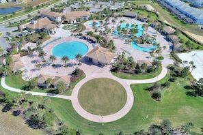 Vista aérea de un complejo turístico con varias piscinas, un césped circular en el centro y villas circundantes.