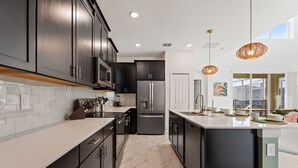 Una cocina moderna con armarios oscuros, un refrigerador de acero inoxidable y una isla grande con pileta.