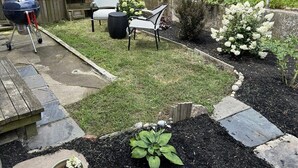 A backyard with a barbecue grill, outdoor seating, and a garden with white flowers. - Cozy two bedroom house in the heart of Gloucester (Gloucester)