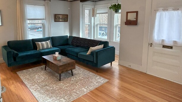 A living room with a sectional sofa, a wooden coffee table, and a ceiling fan. - Cozy two bedroom house in the heart of Gloucester (Gloucester)