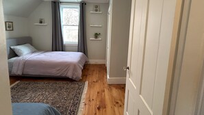 A bedroom with a bed, a ceiling fan, a window with curtains, a door, and a small shelf with a plant. - Cozy two bedroom house in the heart of Gloucester (Gloucester)