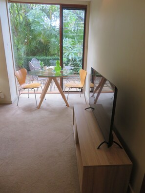 Een moderne woonkamer met een glazen tafel, twee oranje fauteuils, een houten tv-meubel en een grote schuifpui naar een tuin.