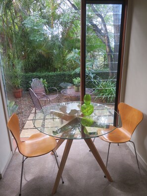 Een glazen tafel met twee stoelen in een kamer met uitzicht op een weelderige tuin door een raam.