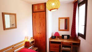 Un dormitorio con cama, armario de madera, escritorio, silla, lámpara y ventana con cortinas.