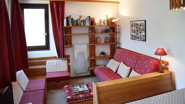 Una habitación acogedora con un sofá de madera, dos sillones a juego, una mesita y una estantería llena de libros y objetos decorativos.